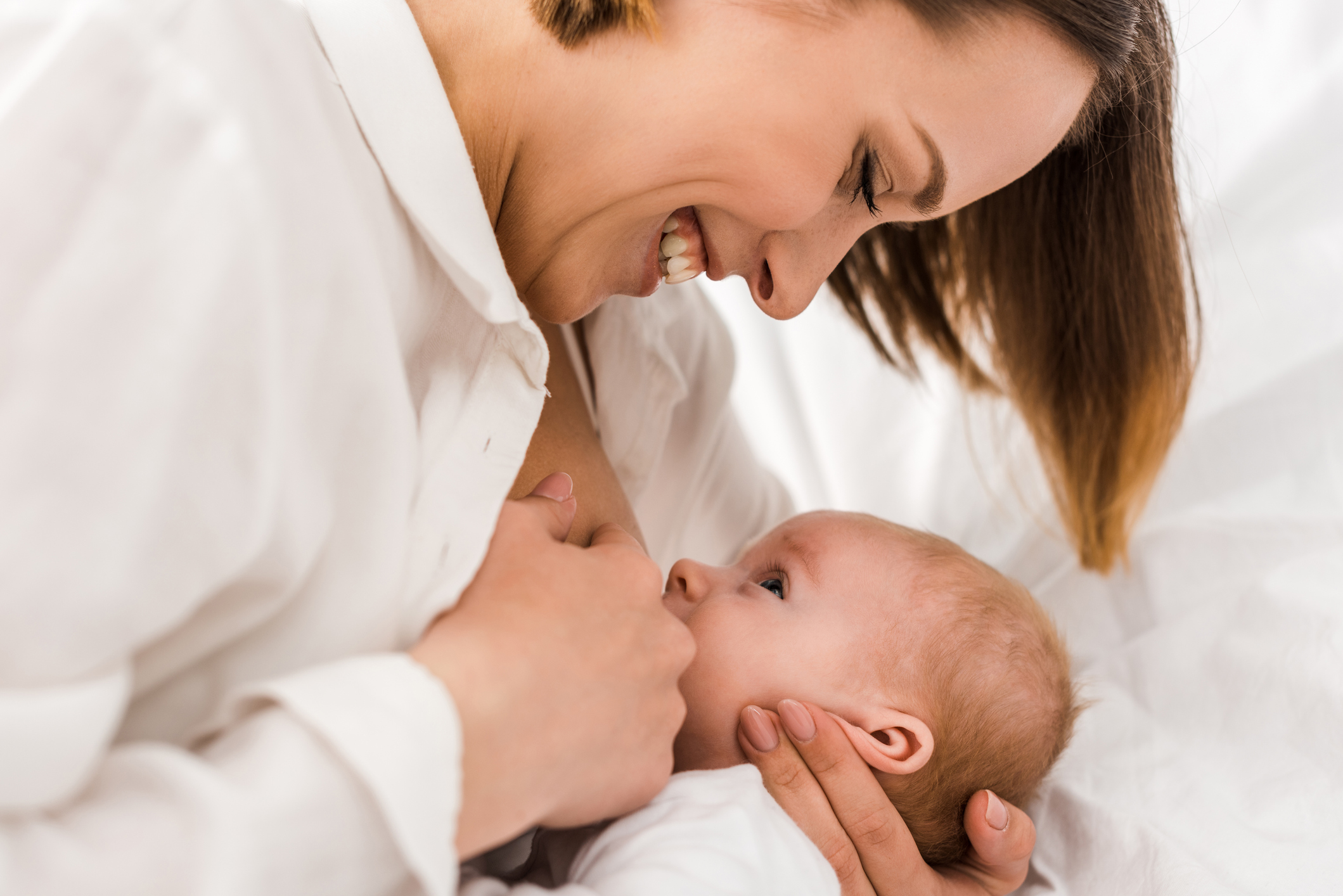 A happy woman in a white shirt breastfeeds her newborn