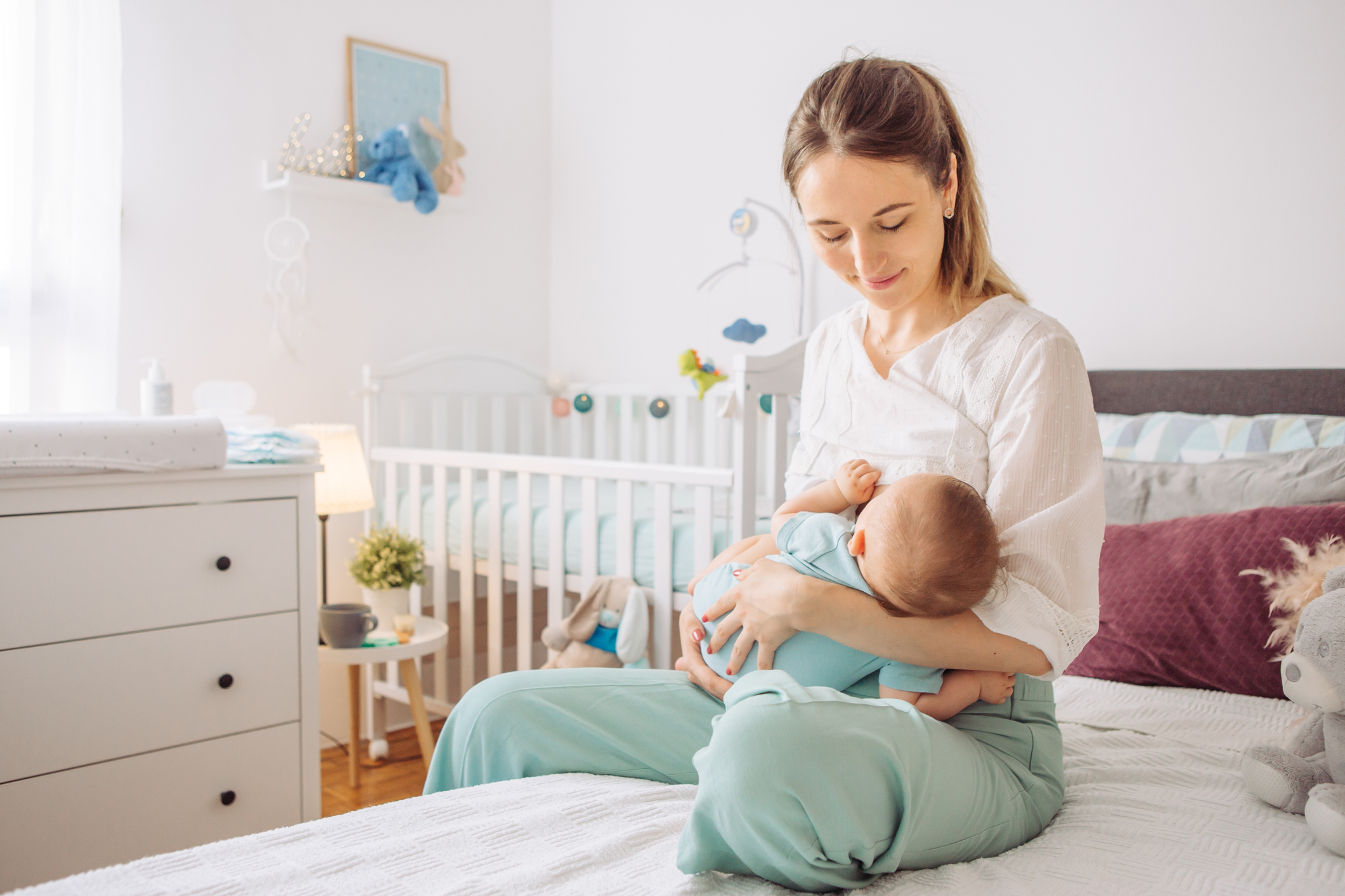 A young mom breastfeeds her baby in the nursery of her home