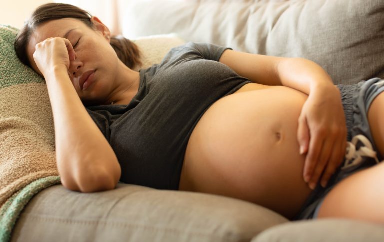 A uncomfortable pregnant woman rests at home, lying on her couch.