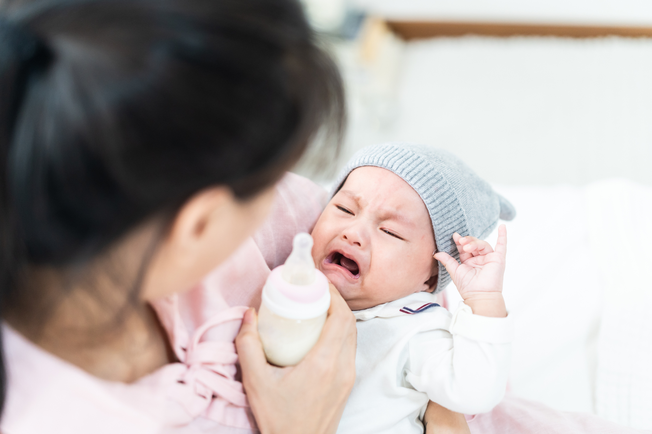 A newborn baby cries while trying to drink a bottle