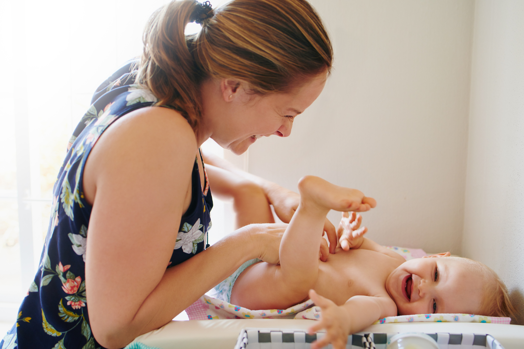 A woman tickles her baby on the changing table