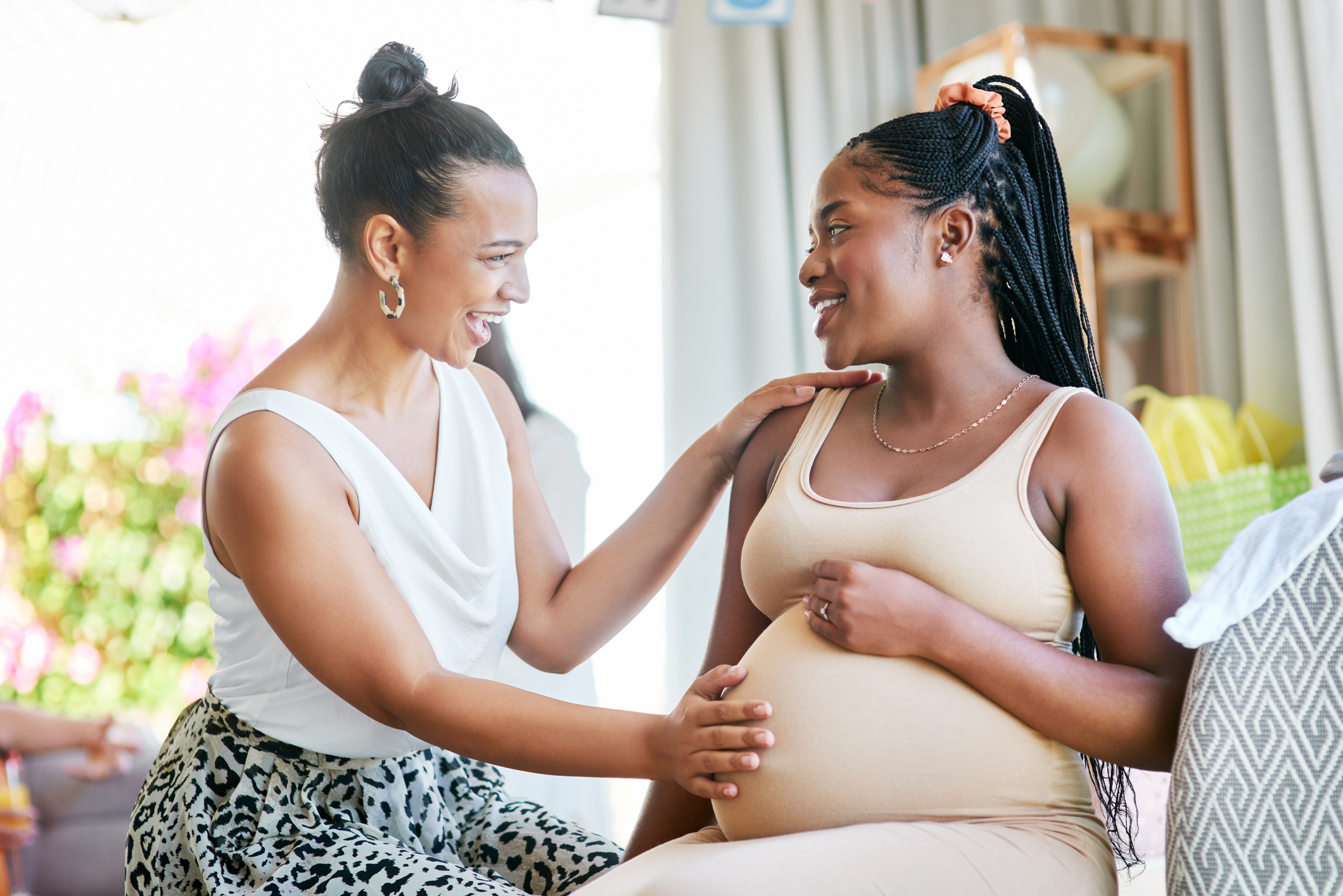 A woman touches her pregnant friend's belly while they smile