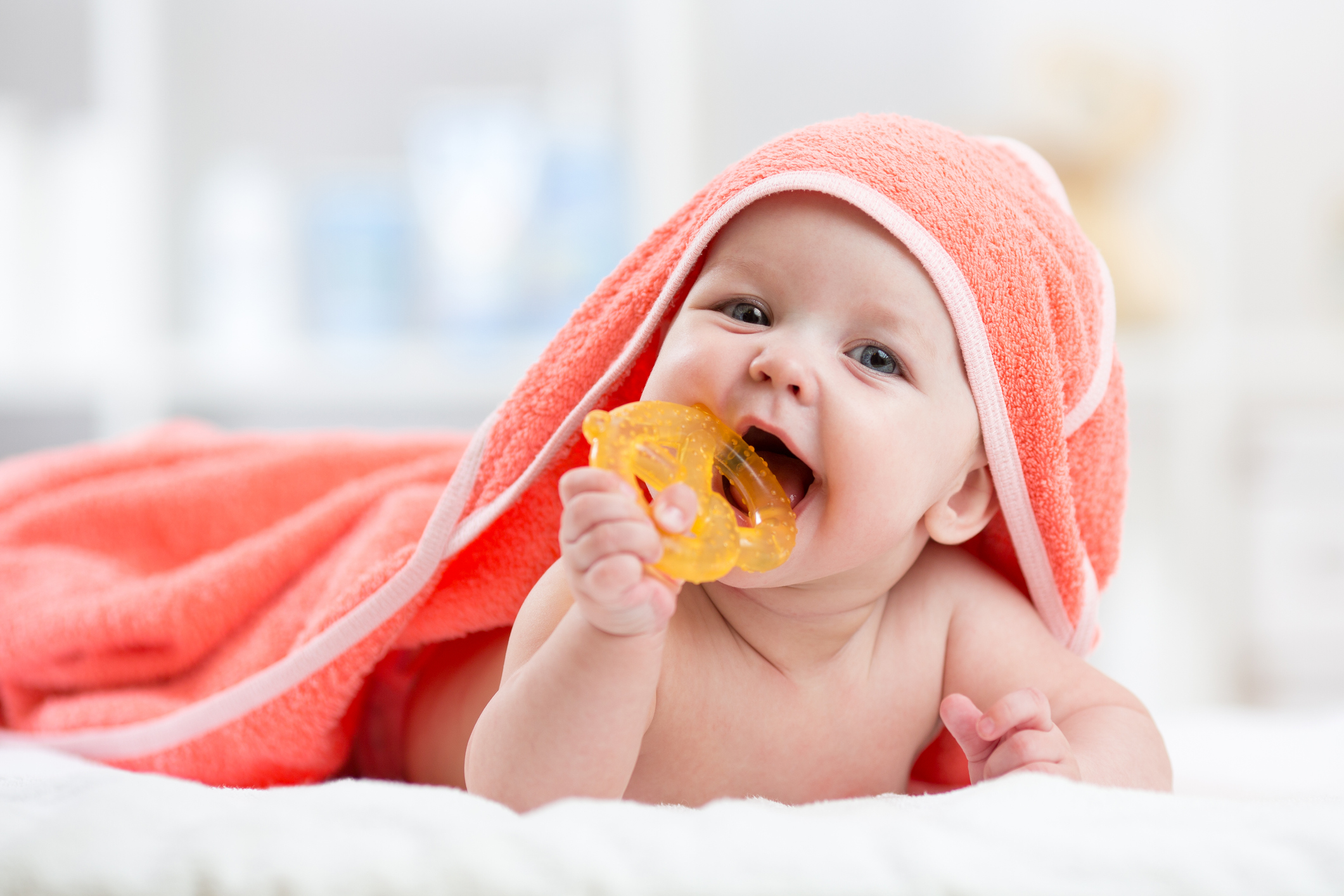 A baby covered in a towel chews on a teething toy