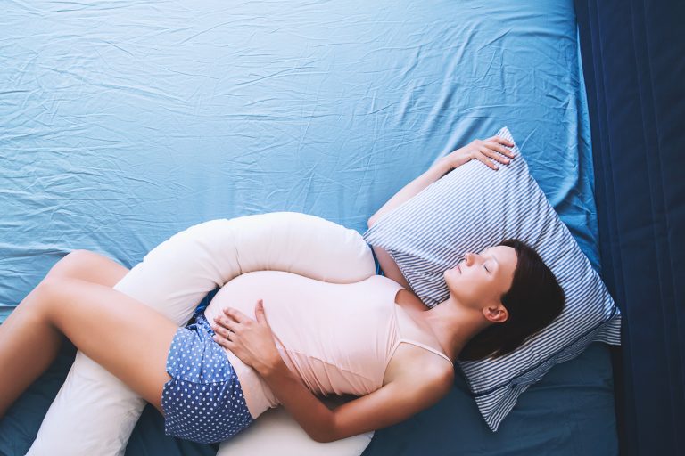 A pregnant woman sleeps with a body pillow
