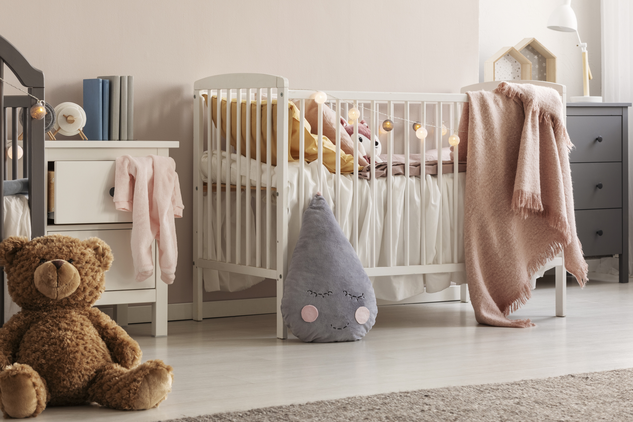 Blush pink nursery with a crib and stuffed bear in the corner