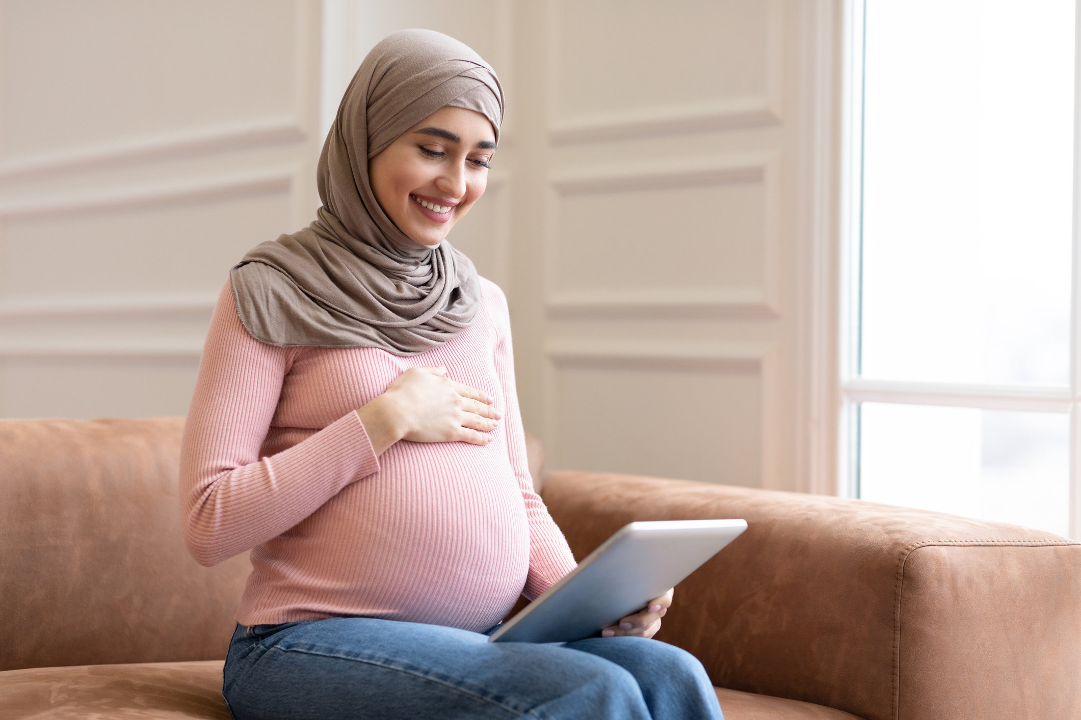 Happy Muslim pregnant woman looks at a tablet computer