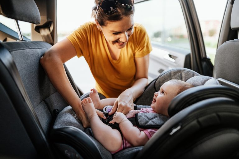 A mom puts her happy baby into a carseat
