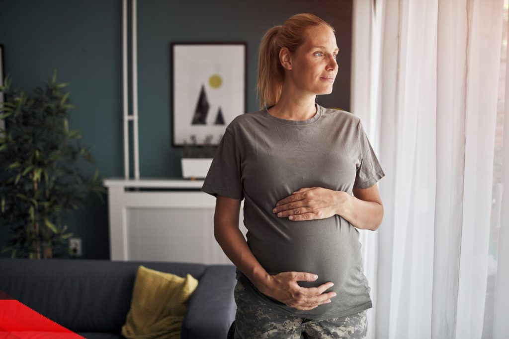 A pregnant woman looks out a window at her home