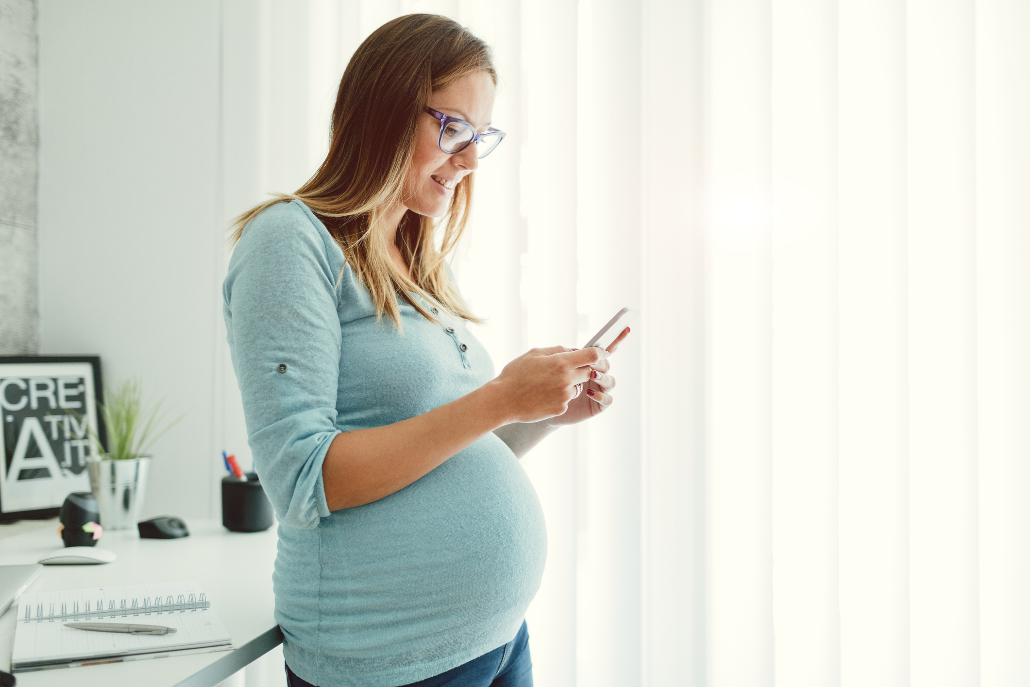 A smiling pregnant woman looks at her smart phone