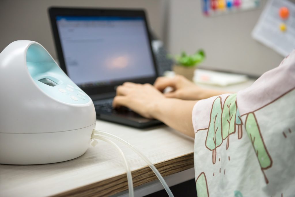 A mom pumps breastmilk at a computer with an automatic spectra