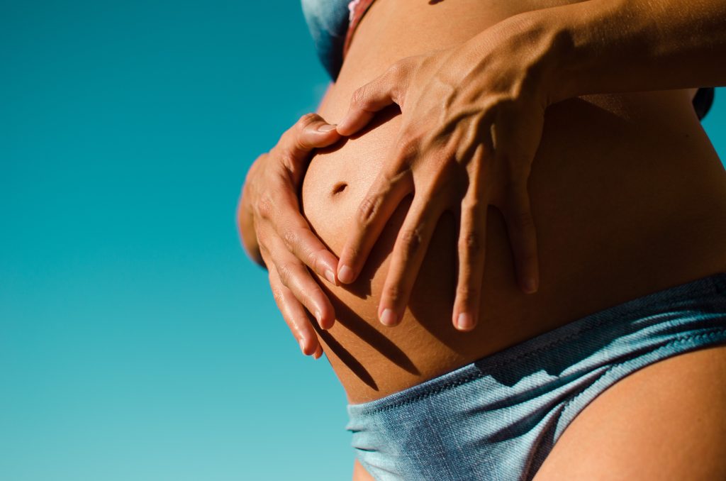 A pregnant woman in a bikini makes a heart with her hands on her belly