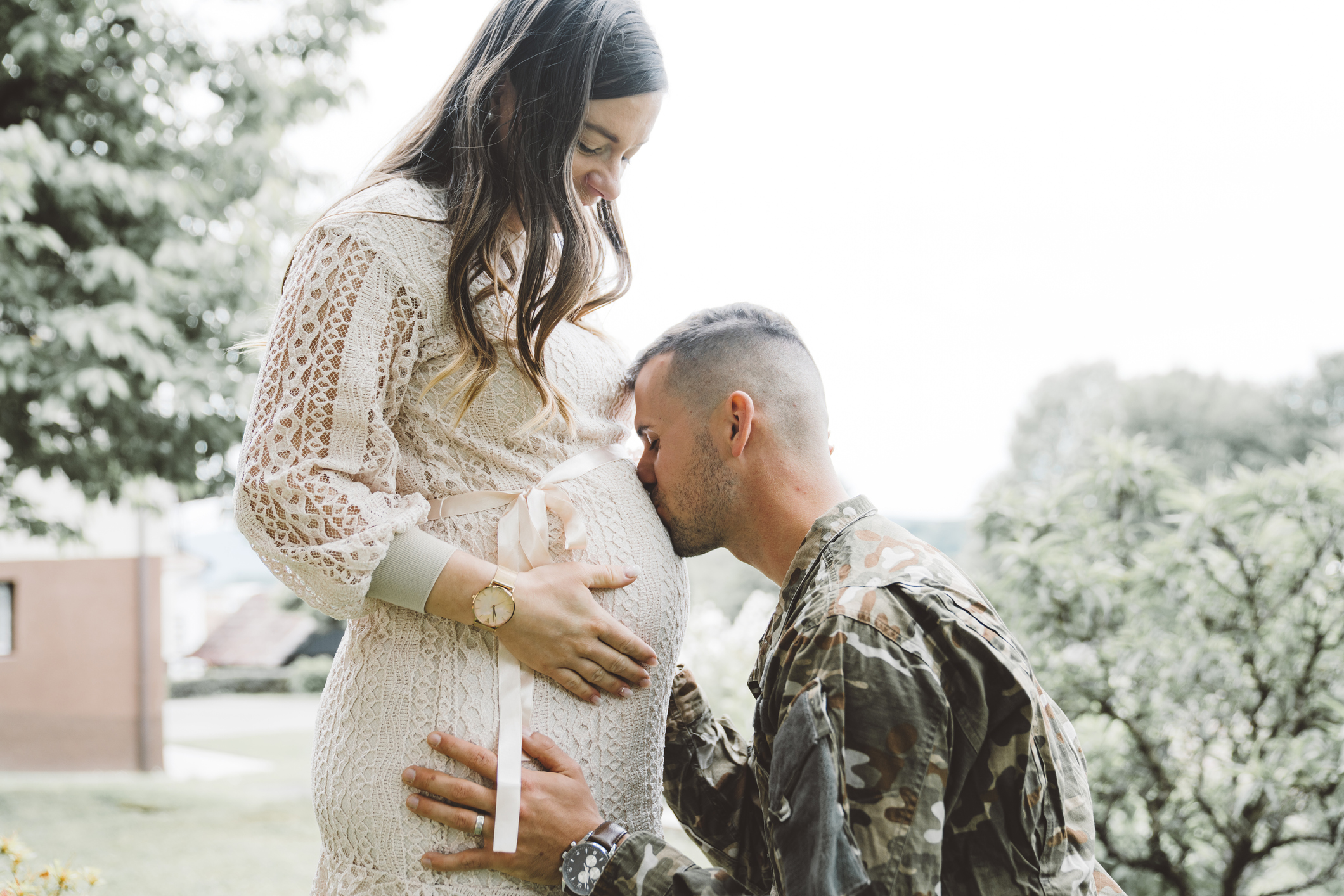 Man in army uniform kissing his pregnant wife belly