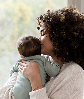 A young mom smiles and smells her baby's head