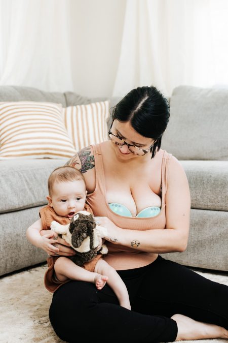 Mom wearing Motif Aura breast pump holding her baby