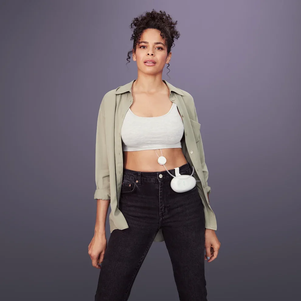 Mom standing hands free with the Elvie Stride under her top and the hub clipped to her jeans